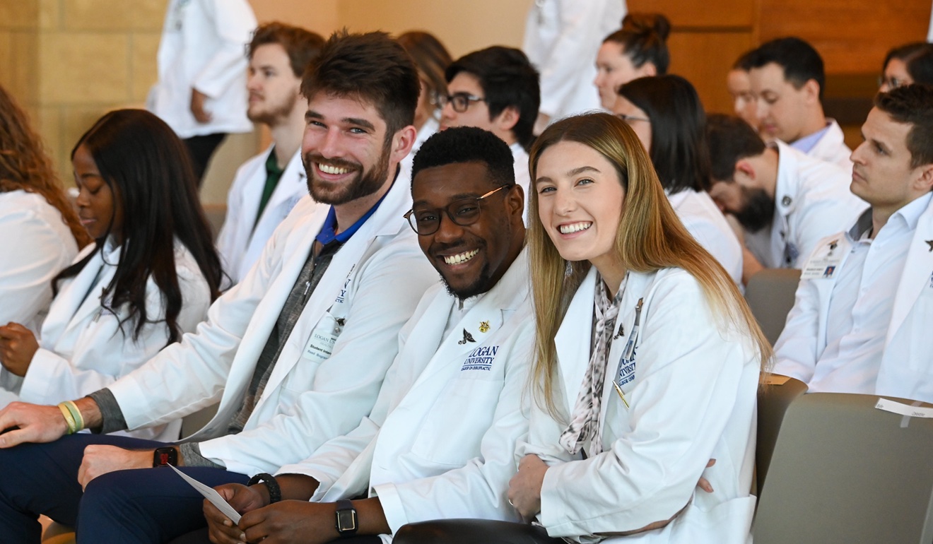 three students in white coats smiling